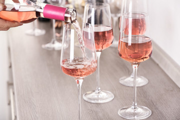 Canvas Print - Young woman pouring delicious rose wine from bottle into glass on wooden counter, closeup