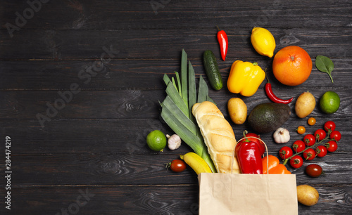 Cuadros en Lienzo Shopping paper bag with different groceries on dark wooden background, flat lay