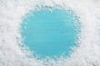 Frame of white snow on light blue wooden background, top view with space for text. Christmas season
