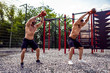 © zamuruev - Two Athletic men working out with a kettlebell at street gym yard. Strength and motivation. Outdoor workout.