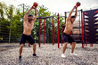 © zamuruev - Two Athletic men working out with a kettlebell at street gym yard. Strength and motivation. Outdoor workout.