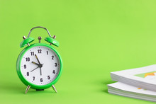 Green Alarm Clock With Stack Of Financial Documents On Green Background