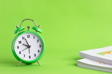 Green alarm clock with stack of financial documents on green background