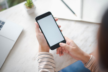 Closed up and focus on hand of young woman using a smartphone which show white display and have notebook put on table in near. see from top view. co working space concept.