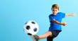 Boy playing soccer kicking the ball on blue background