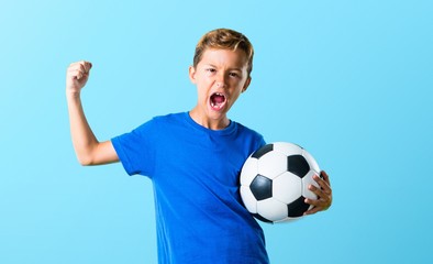 Wall Mural - Lucky boy playing soccer on blue background