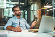 © Friends Stock - Business talk. Young and successful bearded man in eyeglasses and headphones talking with client by phone while sitting in the modern office