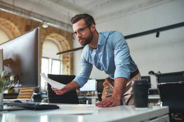 working all day. young bearded businessman in eyeglasses and formal wear using computer while standi