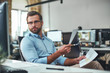 © Friends Stock - Examining the reports. Busy and focused bearded man in eyeglasses and formal wear holding documents and looking at computer monitor while sitting in the modern office