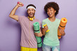Photo of happy guy and woman work on biceps with weights, carry karemats, have joyful expressions, enjoy training together, dressed in casual wear, being motivated for healthy lifestyle and sport