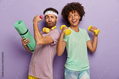 Fotografía Glad multiethnic husband and wife attend sport center, exercise with dumbbells,