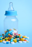 Fototapeta  - Concept of baby taking pills. Baby`s milk bottle full of pills and capsules against the blue background
