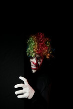 Scary Clown Peeping Around The Corner Of A Black Wall. He Is Wearing A Colored Wig And Sharp Fangs.