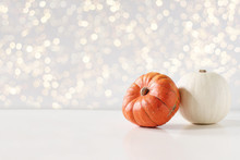 Modern Autumn Styled Composition. White And Orange Pumkins On White Table Background. Halloween, Thanksgiving Party Concept. Festive Fall Design With Golden Sparkling Bokeh Lights. Empty Space.