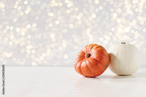 Modern autumn styled composition. White and orange pumkins on white table background. Halloween, Thanksgiving party concept. Festive fall design with golden sparkling bokeh lights. Empty space.