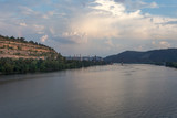 Fototapeta Desenie - Large river flowing towards factory at edge of mountain