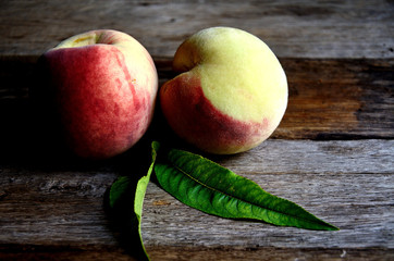 Two ripe peaches with leaves lie on old wooden boards.