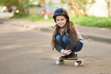 A little girl squats on a skateboard.