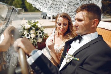 Wall Mural - Beautiful bride in a long white dress. Handsome groom in a black suit. Couple sitting in a car