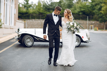 Wall Mural - Beautiful bride in a long white dress. Handsome groom in a black suit. Couple near old car