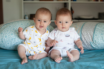 Happy fraternal twins sisters with pajamas laughing in bed at home.. Family at home.