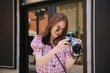 © Somkiat - Young attractive woman in stylish sunglasses checking photos on retro equipment standing at street in the city.
