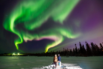 Two girls look northern lights, which stretches beyond horizon