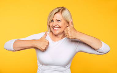 Big win! Happy excited smiling beautiful senior woman shows thumbs up and looks on camera