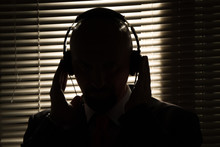 Bald Man With Headphones On The Background Of Closed Blinds, Contour Lighting, Listening To Music On Old Equipment