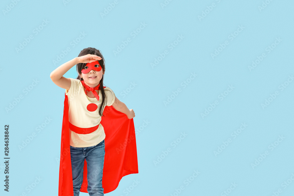 Cute little girl dressed as superhero on color background