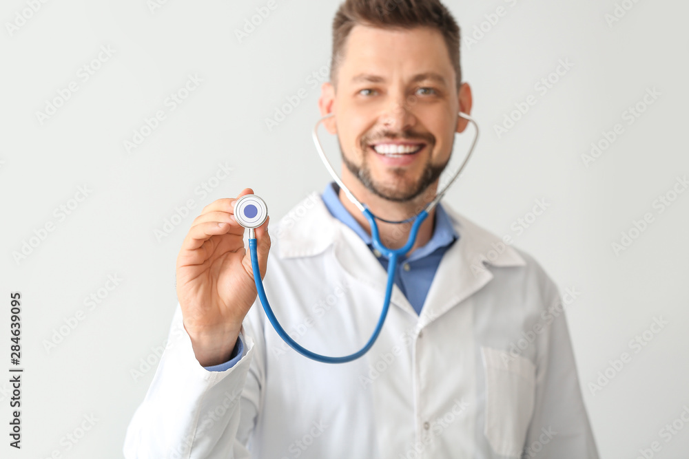 Male doctor with stethoscope on light background