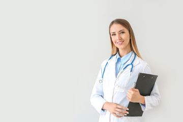 Female doctor with stethoscope and clipboard on light background