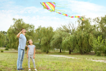 Poster - Young man with little daughter flying kite outdoors