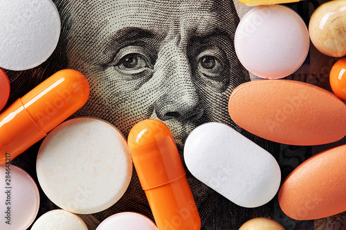 Capitalism and healthcare policy concept. Colorful medical pills cover Benjamin Franklin\'s face on one hundred american dollar bill. Macro top down view.