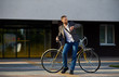 © oes - A young stylish bearded  businessman in suit going to work by bike. Drinking coffee from a cup to go and talking on a mobile  phone on the background of an office building. Takes a working break