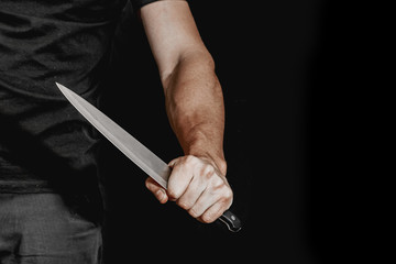 Man's hand holds a knife on black background. topics of violence and murder. thief, killer, rapist, maniac