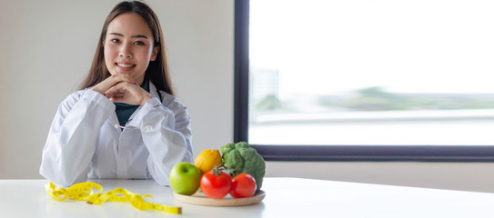 panoramic view young pretty nutritionist female doctor or medical smiling and looking at camera with fresh vegetables on desk at laboratory office, nutrition, lifestyle, healthy food, dieting concept