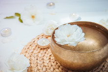 Close Up Tibetan Singing Bowl With Floating In Water Rose Inside. Burning Candles, Flowers Petals On The White Wooden Background. Meditation And Relax. Exotic Massage. Copy Space.