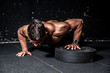 © Srdjan - Young strong sweaty focused fit muscular man with big muscles performing push ups with one hand on the barbell weight plate for training hard core workout in the gym