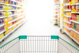 Fototapeta  - Empty shopping cart or pushcart in supermarket aisle. Buying goods or products in grocery store. Shopping concept