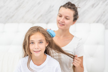 Happy young mother is combing her daughter at home