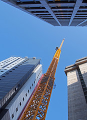 Wall Mural - vertical view of a tall yellow construction crane working on a new concrete building with large surrounding towers