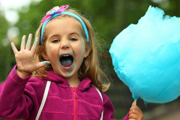 Wall Mural - Closeup portrait of happy toddler girl eating bright blue cotton candy