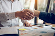 © wutzkoh - Entrepreneurs collaboration deal shaking hands in a modern office and financial paper graph on desk.