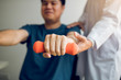 © wutzkoh - Asian physiotherapist helping a patient lifting dumbbells work through his recovery with weights in clinic room.