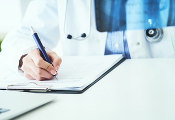 Close up of female doctor holding x-ray or roentgen image and making notes in medical form.