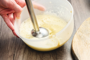 close-up whipping the mixture of homemade mayonnaise with a blender in a plastic bowl