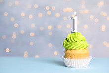 Birthday Cupcake With Number One Candle On Table Against Festive Lights, Space For Text