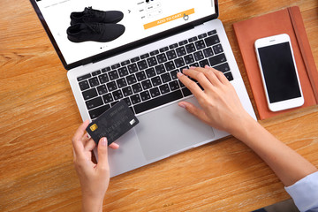 Canvas Print -  Business woman using credit card for buy black running shoes on ecommerce website via laptop with smartphone and note book on wooden desk