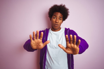 Canvas Print - Young african american man wearing purple sweatshirt standing over isolated pink background Moving away hands palms showing refusal and denial with afraid and disgusting expression. Stop and forbidden